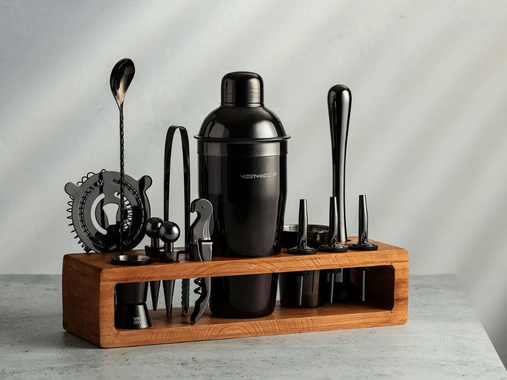 Set of bar tools including a black cocktail shaker on a wooden stand with a neutral background